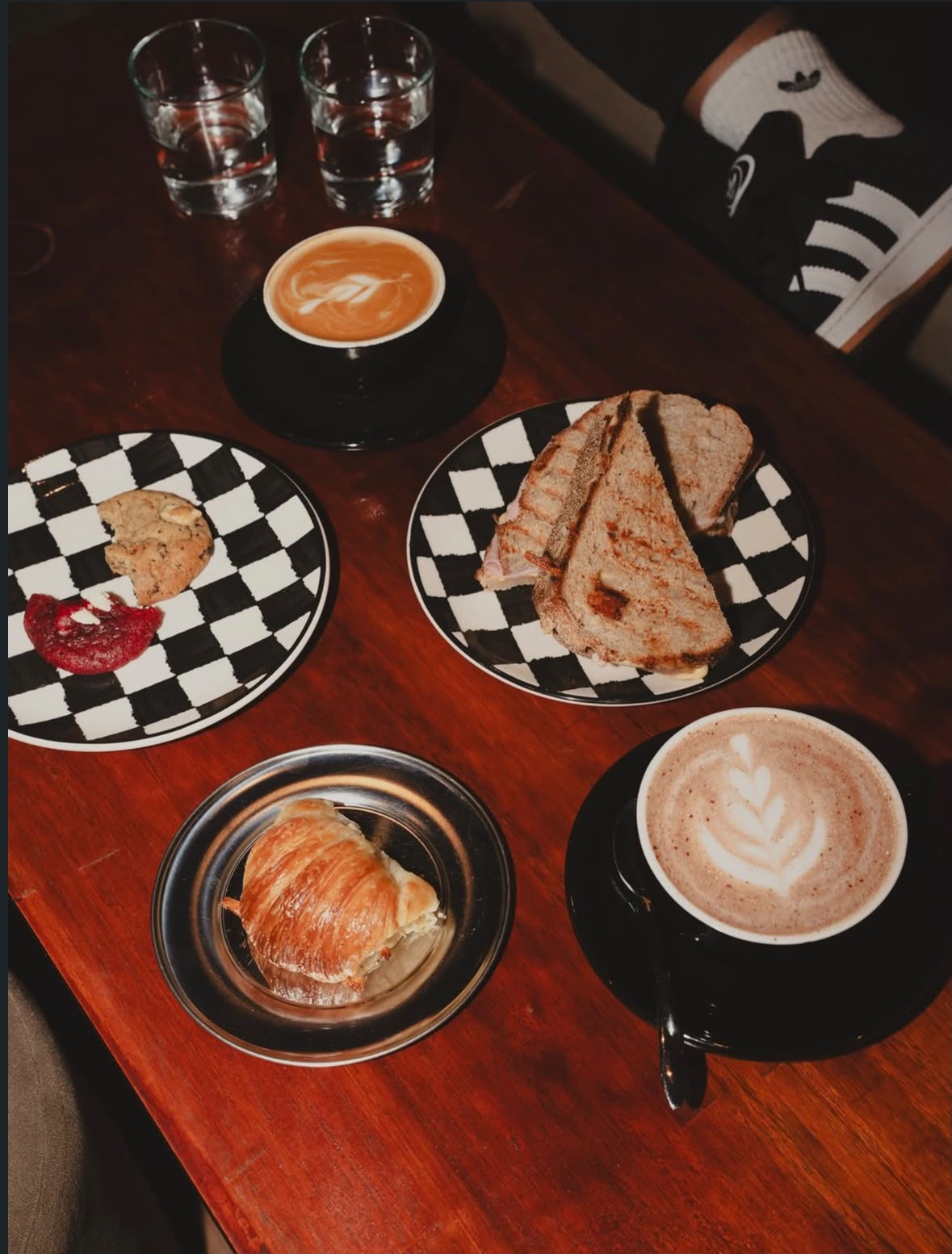 Mesa con dos cafés con latte art, tostado, croissant y cookies