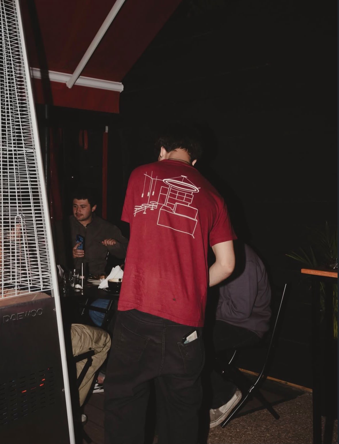 Remera bordó con el dibujo del local, en la vereda de noche